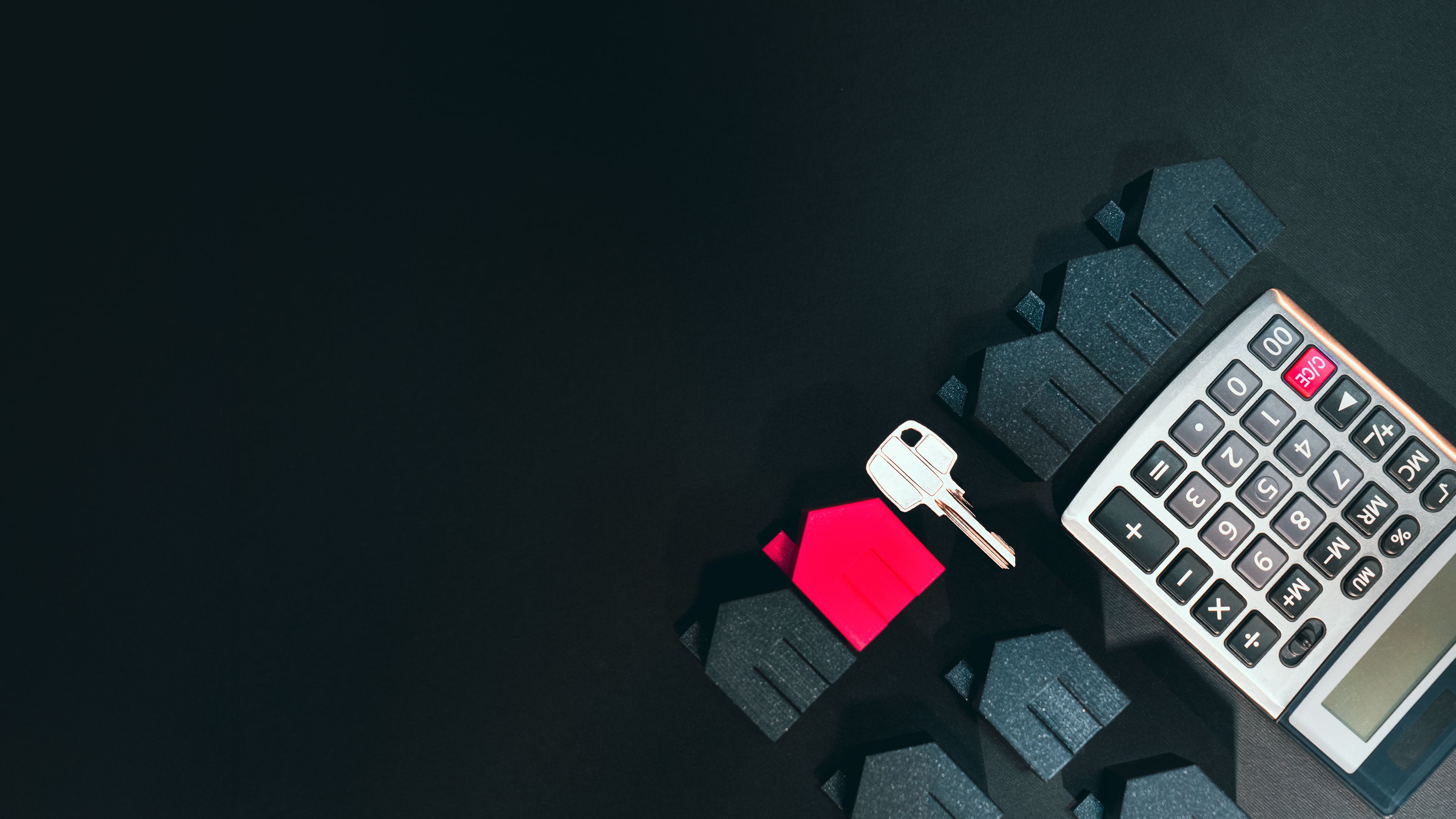 Calculator, house key and model homes on a dark surface.